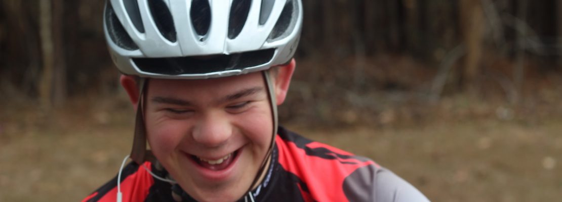 Young man with down syndrome smiling while sitting on his bike.